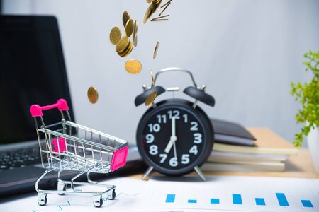 Falling gold coins in shopping cart or supermarket trolley on working table with office supplies or office work essential tools items for business financial conceptの写真素材