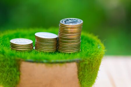 Stack of gold coin  on artificial grass in pot, on wooden table with green nature background. shallow focus. business success and banking concept.の写真素材