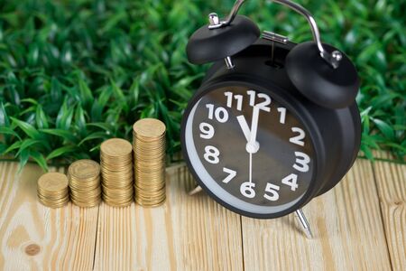 Steps of coins stack with vintage alarm clock on wooden working table with copy space for text,...