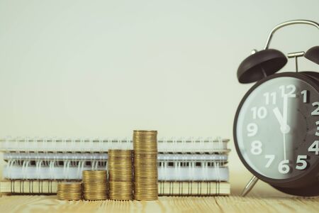 Steps of coins stack with vintage alarm clock and pen, notebook paper on wooden working table with...