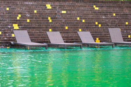 Deck chair or sunbath near private swimming pool with sun umbrella and exotic plants garden,...