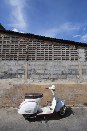 white Classic Vespa scooter stands parked near the concrete old wall,white Vespa scooter stands parked near the concrete old wall with blue sky background,white Classic Motorcyclesの写真素材