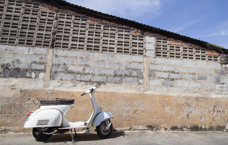 white Classic Vespa scooter stands parked near the concrete old wall,white Vespa scooter stands parked near the concrete old wall background,white Classic Motorcycles stands parked near the concrete old wall backgroundの写真素材