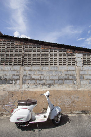 white Classic Vespa scooter stands parked near the concrete old wall,white Vespa scooter stands parked near the concrete old wall with blue sky background,white Classic Motorcyclesの写真素材