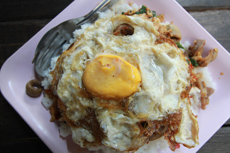 fried basil leaf with chicken and fried eggs on rice in wooden backgroundの写真素材