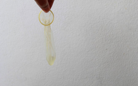 Used condom in hand on white wall background.の写真素材