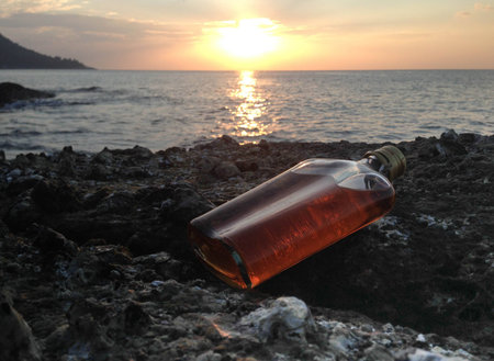 whisky in flat Bottles on rock beach with sunsetの写真素材