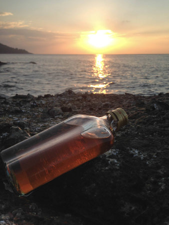 whisky in flat Bottles on rock beach with sunsetの写真素材