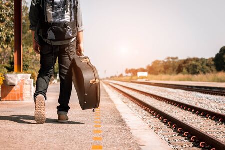 Backpacker is holding guitar case at railway station.の写真素材