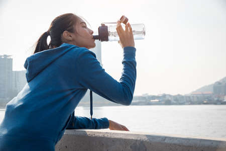 Tired Young woman is drinking water after run in the morning.の写真素材