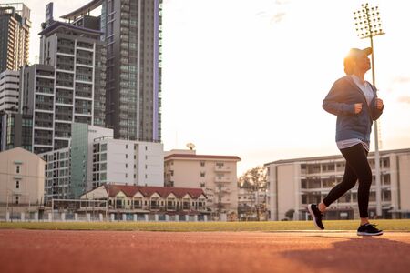 Young woman is running on racetrack at sunset, building behind.