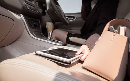 Businesswoman holding digital tablet while driving in car, using communication for work.