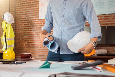 Engineer is holding blueprint and safety helmet in office