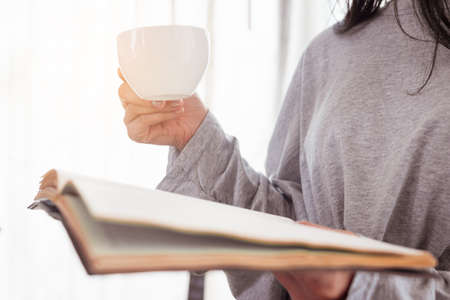 Close up woman hand is holding a cup of coffee and reading book.