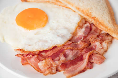 Close up breakfast with sunny side eggs, bacon and toast bread on a plateの写真素材