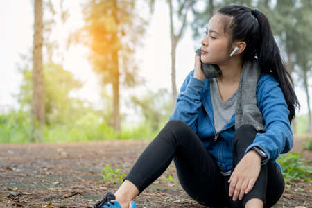 Tired young Asian woman is wiping her sweat after run in the morning.の写真素材