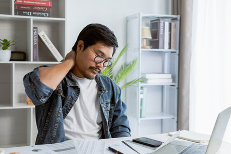 Overworked man is suffering from office syndrome. Tried male has severe neck pain while working.