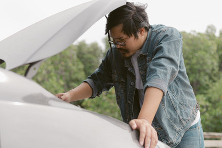 Asian male is checking inside car bonnet after car breakdown. Man driver is trying to repair a car engine.の写真素材
