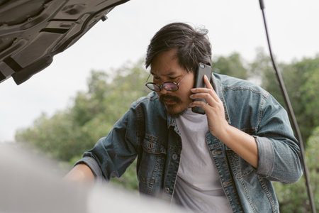 Man driver is using a mobile phone to call for help after car breakdown.の写真素材
