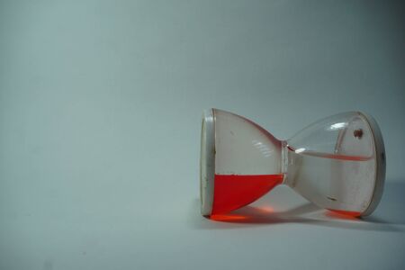 sand clock is laying down some red liquid inside it with white background