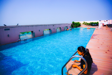 india - jaipur - hotel royal orchid - september 9, 2019, a roof top swimming pool is built, it is fills with deep blue water and a girl is sits near it and some people are in the poolのeditorial素材