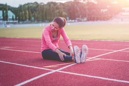 Beautiful woman fitness runner stretching legs before run,worm up body in stadium.