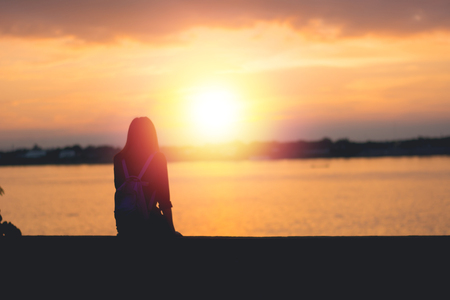 Silhouette of woman sitting riverside and beautiful sunset background.の写真素材