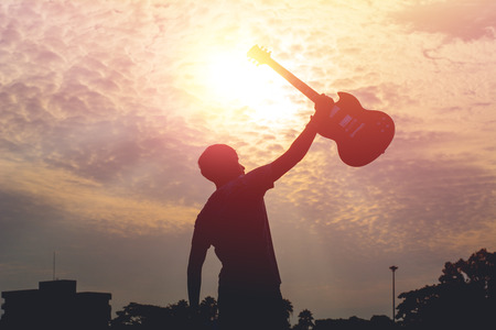 Silhouette of young musician holding a guitar on sunset.の写真素材