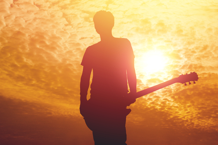 Silhouette of young musician holding a guitar on sunset.の写真素材