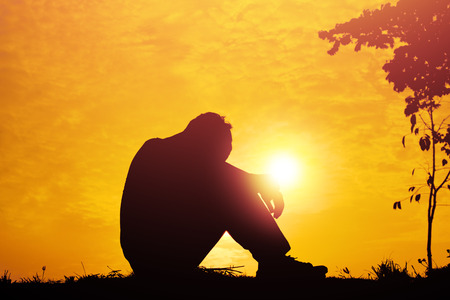 Silhouette of a young boy sitting sadly on sunset.の写真素材