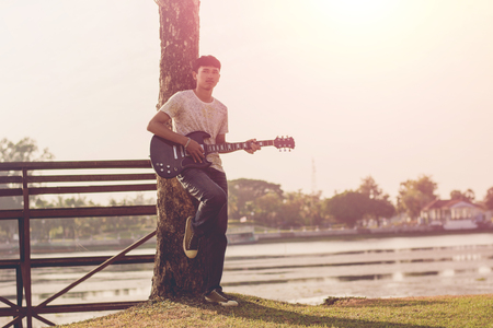 Young hipster man playing guitar to relaxing on his holiday, enjoy with natural and fresh air.の写真素材