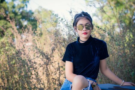 Fashion pretty young woman model in hipster style,fashion black glasses,stands over forest background. Outdoor portrait of cute girl having fun.の写真素材