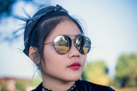 Fashion pretty young woman model in hipster style,fashion black glasses,stands over forest background. Outdoor portrait of cute girl having fun.の写真素材