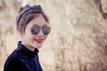 Fashion pretty young woman model in hipster style,fashion black glasses,stands over forest background. Outdoor portrait of cute girl having fun.の写真素材