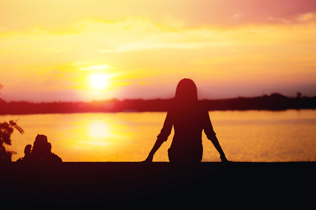 Silhouette of woman sitting riverside and beautiful sunset background.の写真素材