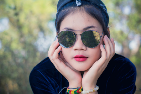 Fashion pretty young woman model in hipster style,fashion black glasses,stands over forest background. Outdoor portrait of cute girl having fun.の写真素材