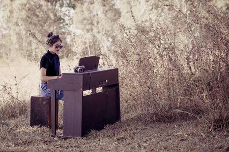 Fashion pretty young woman model in hipster style ,fashion black glasses and vintage camera, she play piano in forest background.の写真素材