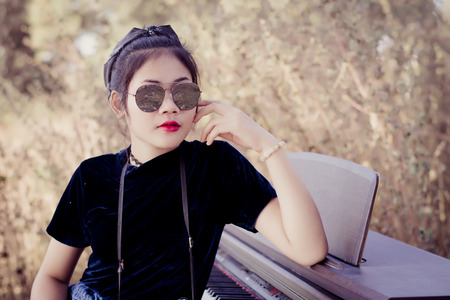 Fashion pretty young woman model in hipster style with piano and vintage camera ,fashion black glasses.の写真素材