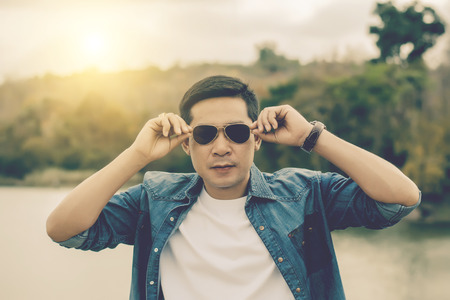 Seductive young man holding sunglasses. smiling and looking at camera over in the outdoor background.の写真素材