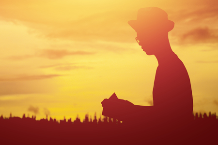 Silhouette of young man reading a book on the riverside park in free time.の写真素材