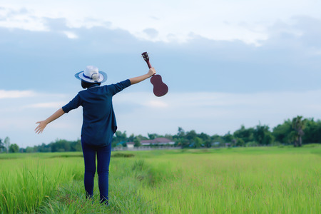 Woman holding ukulele and raise two arms embrace  summer sky with puffy clouds,の写真素材