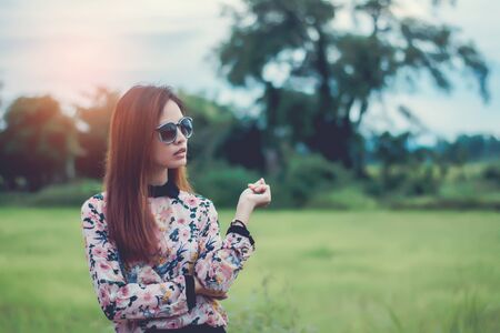 Hipster woman wearing floral shirt ,wears black sunglasses and standing with  a nature background on...