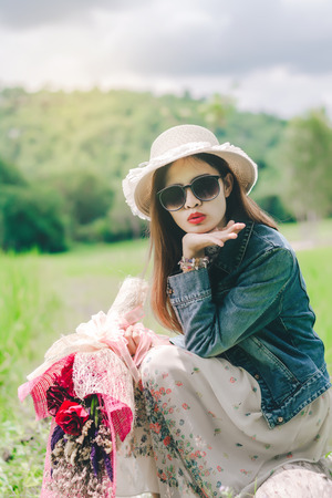 Young beautiful woman dressed vintage and hat classic  with a bouquet of flowers in hands,Black sunglasses,fashion vintage in the meadow.の写真素材