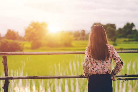 Sad lonely young woman in a field bored with depression,sunset background.の写真素材