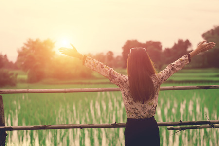 Hipster woman standing stretch her arms in the air on nature. Woman enjoy with nature during sunset.の写真素材