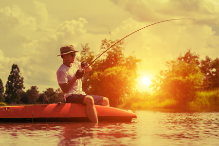 fishing man on board into the river against the background of a picturesque landscape at dawn, on sunset.の写真素材