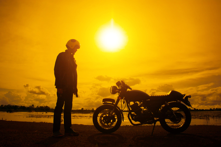 Silhouette of biker man with his motorbike beside the natural lake and beautiful, enjoying freedom and active lifestyle, having fun on a bikers tour.sunset background and sky.の写真素材