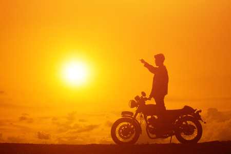 Silhouette of biker man with his motorbike beside the natural lake and beautiful, enjoying freedom and active lifestyle, having fun on a bikers tour.sunset background and sky.の写真素材