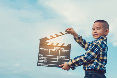 Kid playing film clapper board against summer sky background. Film director concept.の写真素材
