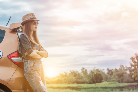 Woman traveler leaning against on car,wearing a  brown hat ,she was wearing jeans,on sunset background.の写真素材